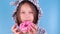 a girl in pajamas eats a pink donut and licks her fingers on a blue background