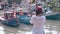 Girl with phone in pictorial bay with fishing boats on day