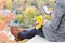 Girl with a phone sits on a hill, yellow leaves in her hand. Autumn on the background