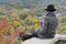 Girl with a phone sits on a hill, yellow leaves in her hand. Autumn on the background