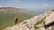 Girl photographer goes up the hill uphill against the backdrop of cliffs of a plateau and the sky with clouds. Concept