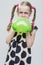 Girl With Pigtails Posing in Polka Dot Dress Against White. Blowing Up Green Heart Shaped Air Balloon.