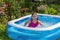 A girl in a pink bathing suit bathes in a blue inflatable pool in a blooming garden