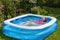 A girl in a pink bathing suit bathes in a blue inflatable pool in a blooming garden