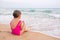 Girl in the pink bathing suit sitting on the beach, eating a wafer and looks into the distance