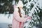 Girl in pink coat in snow Park. Girl plays in winter Park. Adorable child walking in snow winter forest touch wood branch on tree.