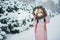 Girl in pink coat in snow Park. Girl plays in winter Park. Adorable child walking in snow winter forest touch wood branch on tree.