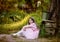 The girl in a pink dress sits in a summer garden at an old well
