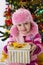 Girl in pink fur hat holding present under Chritmas tree