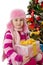 Girl in pink fur hat holding present under Chritmas tree