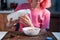 Girl with pink hair pouring milk into the plate with corn flakes