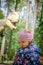 A girl in a pink hat and a colorful jacket walks in the park. Behind her is a huge tyrannosaurus rex