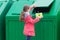 A girl in a pink jacket carries disposable glasses with tubes in a dumpster to throw them away