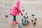 girl in a pink jacket is feeding bread to pigeons Square