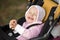 A girl in a pink suit sits in a yellow stroller and smiles, showing recently erupted teeth