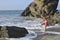 A girl in pink swimming costume on the rocky beach.