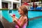 Girl in pink swimsuit enjoys ice cream, records with smartphone by poolside. Young influencer summer fun, live streaming