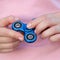 Girl in pink t-shirt is playing blue metal spinner in hands on the street, woman playing with a popular fidget spinner toy, anxiet