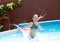 girl playing in outdoor swimming pool jumping into water on summer vacation. Child learning to swim in outdoor pool