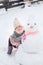 Girl playing with a snowman with pink knitted scarf