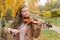 Girl playing the violin in the autumn park on a background of ye