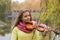 Girl playing the violin eyes closed in the autumn park at a lake and willow foliage background