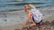 Girl playing with wet pebble stones on coastline. Child washing hands in waves