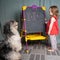 Girl plays at school writes examples on the blackboard and teaches the dog to solve math problems