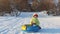 Girl plays with snowtube and hides behind it at hill at sunny winter day