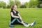 Girl pleased with fitness exercise resting sitting on grass. Nearby is a bottle of water and dumbbells