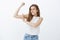 Girl pleased to gain muscles. Portrait of carefree funny european female coworker in tank-top, raising arm and touching