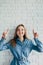 Girl points hands up in a blue shirt against white brick wall and looks thoughtfully to the up with a smile on her face. Place for