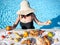 Girl in the pool in a straw hat with assorted breakfast meal and drinks near swimming pool