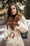 Girl posing on road on winter background. Glamorous funny young woman with smile wearing stylish creamy long fur coat