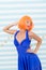 Girl posing striped background of studio. Lady red ginger wig posing in blue dress. Comic actress concept. Woman playful