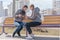 Girl pouring tea from thermos to cup sitting with girlfriend on wooden city bench