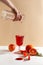 The girl pours juice from a bottle into a glass. Sliced oranges on a white table