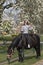Girl on a pregnant brown horse without a saddle, with white blossom in the background, thumbs up