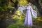 Girl in a princess dress is in a mysterious deep forest with trees, flowers and waterfalls