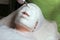 The girl on the procedure in the cosmetology office. Close-up. A beautician in white gloves puts on an alginate mask with a brush