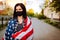 Girl in protective black medical mask wrapped in american flag . Pandemic in quarantine city. Preventing the spread of the