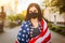 Girl in protective black medical mask wrapped in american flag . Pandemic in quarantine city. Preventing the spread of the