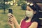 Girl in protective mask holding a smartphone. teen girl siting on bench in green park with mobile phone. First stage of loosening