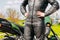 A girl in a protective motorcycle leather suit stands against the background of a motorcycle.