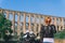 A girl in a protective motorcycle outfit poses against the background of an old Aqueduct of Vanvitelli, Caroline. Sunny day.