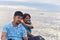 Girl Pulling cheeks of boy while posing for photograph near sea beach. The ocean can be seen in the background.