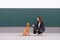 The girl and the puppy sit on the background of the wall. The dog looks into the camera. The owner and cute dog