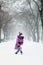 The girl in the purple coat is happy and plays with snow in winter