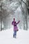 The girl in the purple coat is happy and plays with snow in winter