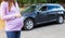 A girl in a purple sweater with a big belly on the background of a car. The concept of traveling by car during pregnancy